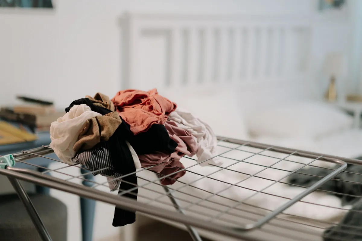 Pile of clothes on a drying rack in a cozy bedroom setting with natural light.