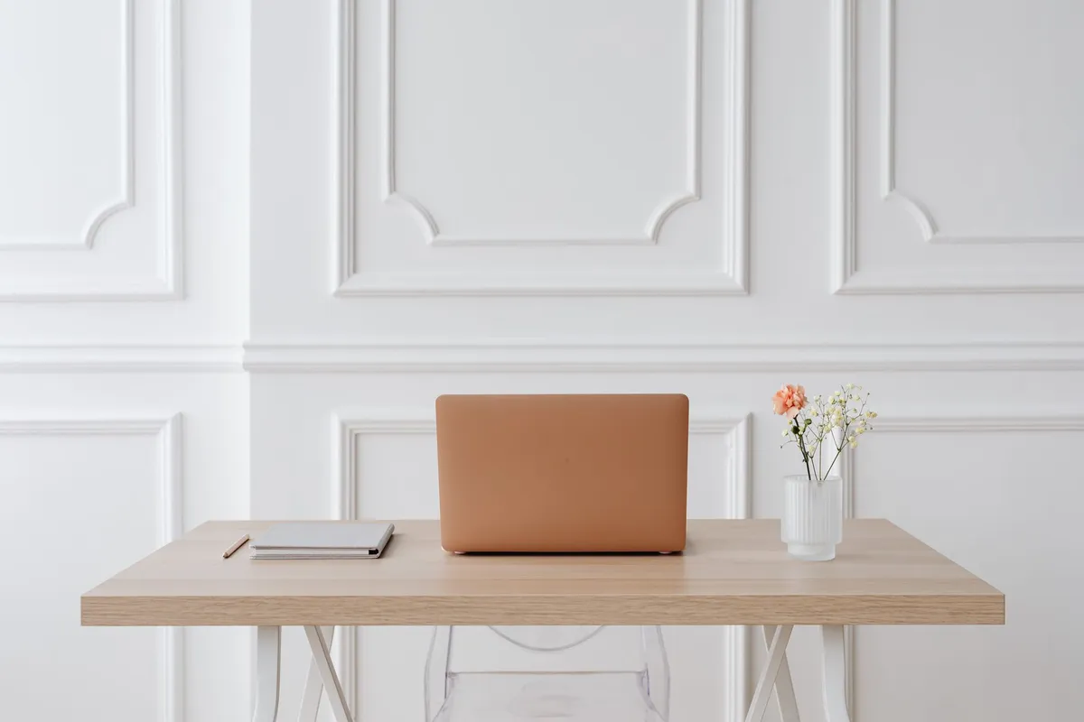 A serene workspace featuring a simple desk with a laptop, notebook, and a vase of flowers.